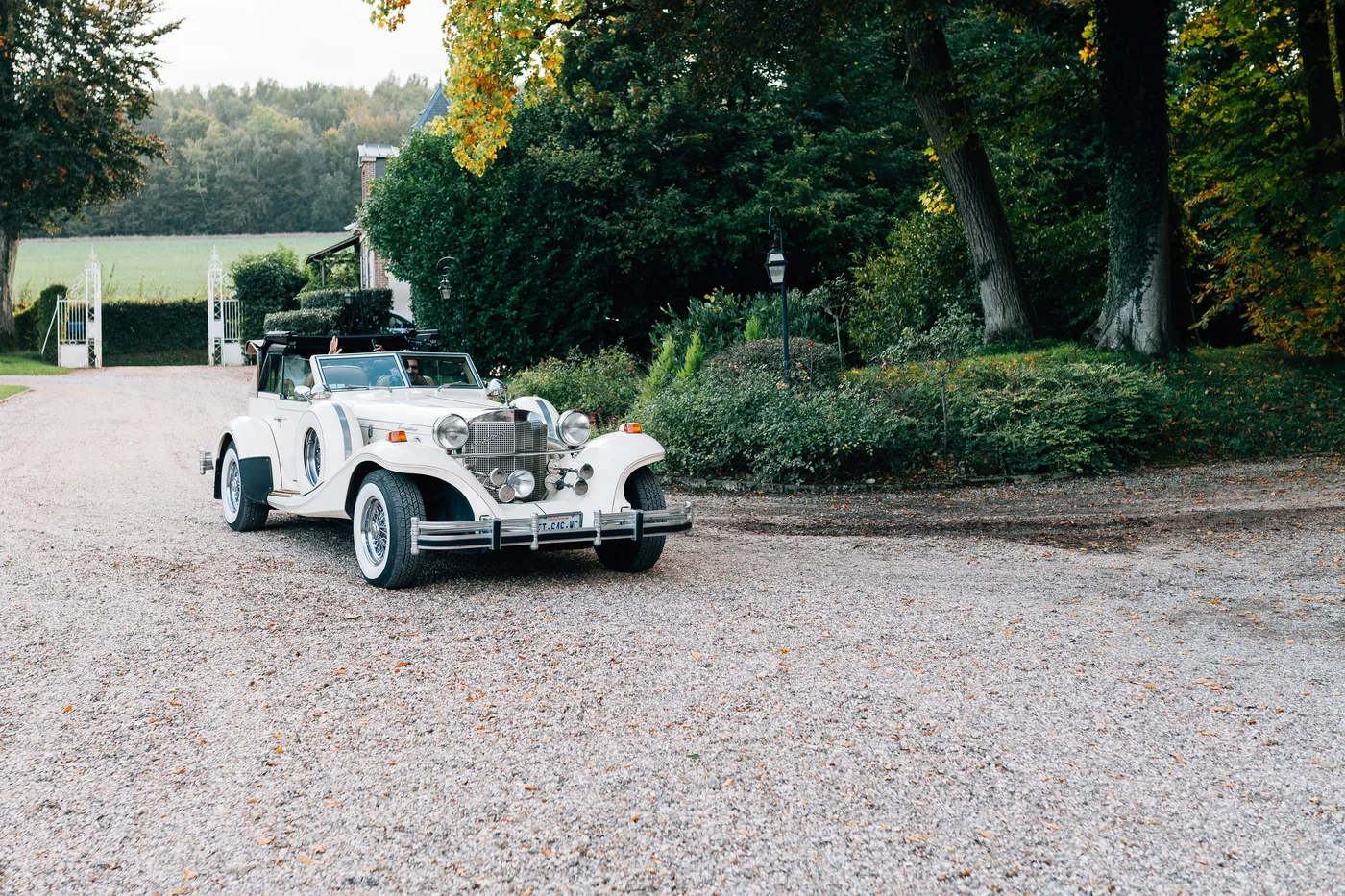 Voiture ancienne crème dans une allée gravillonnée pour un mariage.